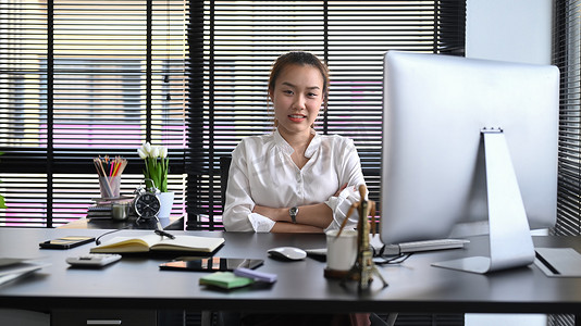 自信的年轻女性企业家坐在她的个人办公室里，对着镜头微笑