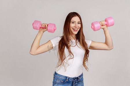 心满意足的女人用粉色哑铃做运动，增强肌肉。