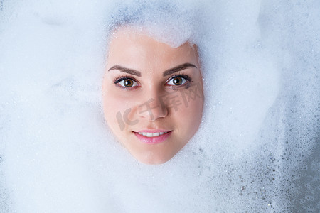脸上的泡沫摄影照片_一个女孩在浴缸里的特写肖像和她脸上的白色泡沫。