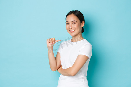 学生找工作摄影照片_身穿白色T恤、自信微笑的亚洲女孩用自豪、自信的表情指着自己，炫耀，提升自己的能力，专业，找工作，站在蓝色背景