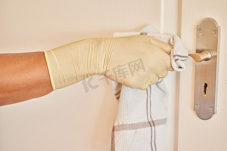 确保新冠病毒不会蔓延。一名面目全非的男子戴着手套，用布清洁家中的门把手。