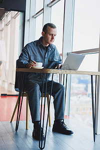 免费沟通摄影照片_一位身穿西装的年轻成功商人喝着咖啡，在咖啡馆里用笔记本电脑无线免费上网工作，独自坐在咖啡馆的桌子旁。