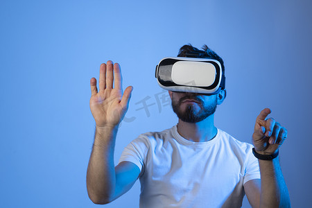 戴着 VR 头盔的留着胡子的年轻男子在彩色背景下玩 VR 游戏。 