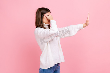 不要生气摄影照片_女性站立的侧视图肖像，伸出手臂，用手掌遮住眼睛，停止手势。
