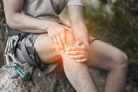 登山摄影照片_在大自然中徒步旅行、攀岩或登山时，一名男子坐在岩石上休息，膝盖受伤和疼痛。 