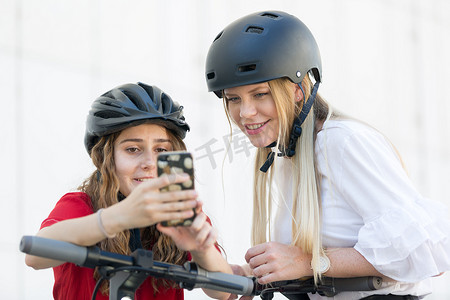 青少年女孩使用移动应用程序在城市环境中解锁和租赁公共租赁电动滑板车。