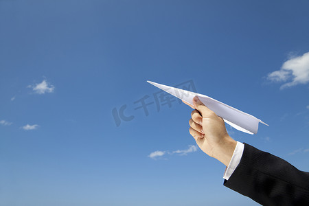 蓝天飞行摄影照片_商人的手让纸飞机飞过蓝天