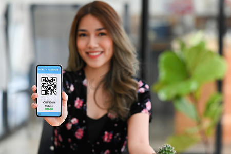 微笑的亚洲女性在屏幕上展示带有疫苗接种认证健康护照的智能手机。