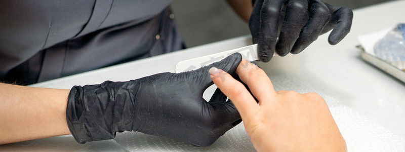 收纳师摄影照片_在美甲沙龙里，一位女士正在接受美甲师用指甲锉修指甲。