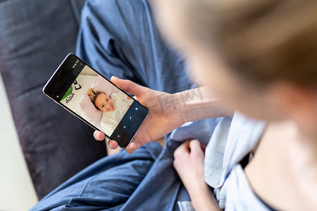 在冠状病毒大流行期间，妇女在家里的沙发上放松，使用手机上的社交媒体与亲人进行视频聊天。