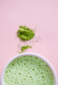 粉红色背景下，一杯白杯生绿茶、泡沫和模糊的日本抹茶粉的部分视图