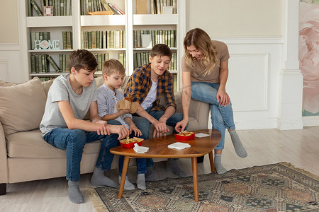幸福的家庭，一个女人和三个十几岁的男孩，坐在客厅的沙发上，吃快餐，装在红盒子里