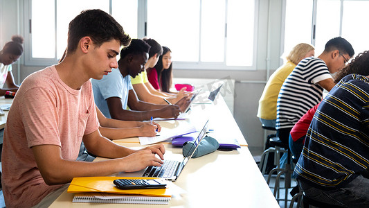 一群多种族高中生在课堂上学习和使用笔记本电脑的侧视图。