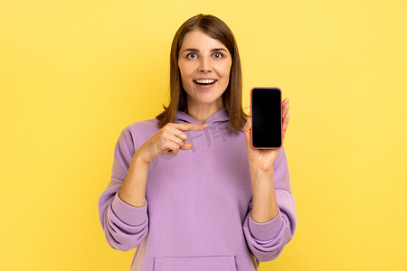 女人指着智能手机，上面显示着空的促销文字，看着相机微笑。
