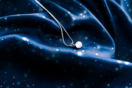 丝绸珠宝摄影照片_深蓝色丝绸上的奢华白金珍珠项链，节日冬季魔法珠宝礼物
