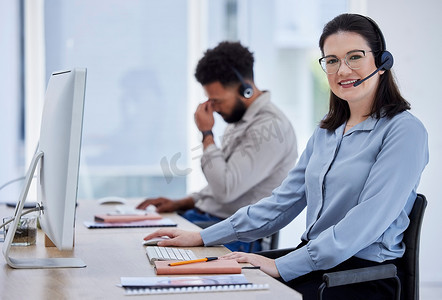 一位快乐的白人呼叫中心电话营销代理在办公室的电脑上工作时戴着耳机交谈，同事在后台的肖像。