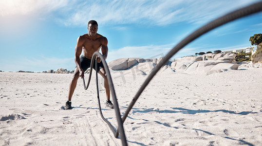 全长健康、活跃的非洲裔美国男子白天使用战绳独自在海滩上锻炼。