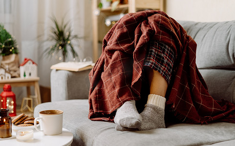 舒适的女性双腿穿着针织冬季温暖的袜子，穿着格子格子花呢，在家里的沙发上休息时喝着杯子里的热可可或咖啡。