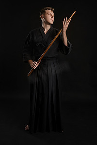 穿着传统日本和服的剑道大师正在黑色工作室背景下用竹剑练习武术。