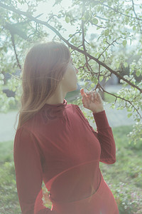 红衣女孩摄影照片_金发碧眼的红衣女孩呼吸着樱花的香味