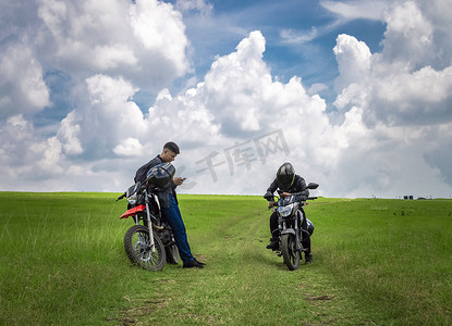 两个男人骑着摩托车停在田野里聊天，两个年轻的摩托车手在田野里，两个骑着摩托车的男人在美丽的乡村道路上，年轻的摩托车手停在路上