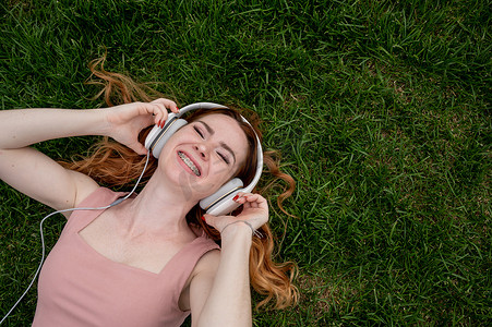 一位年轻的红发女子躺在草地上听音乐。