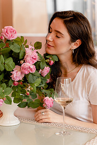 梦想中的女人在夏日露台的咖啡馆里喝着一杯酒精白葡萄酒，桌上放着一束玫瑰。