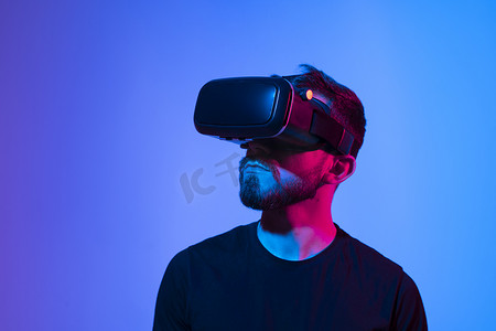 虚拟现实现实摄影照片_惊讶的留着胡子的年轻男子，戴着高科技智能 vr 护目镜，观看 360 度视频或在元宇宙中玩电子游戏。