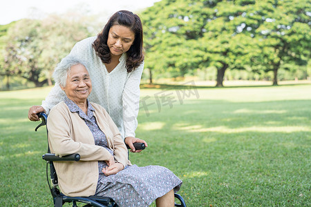 轮椅下坡摄影照片_护理人员帮助和照顾坐在公园轮椅上的亚洲老年或老年老妇患者，健康强大的医疗理念。