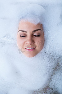 脸上的泡沫摄影照片_一个女孩在浴缸里的特写肖像和她脸上的白色泡沫。