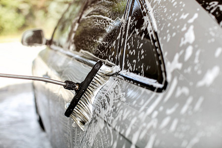 银色汽车的侧面在自助洗车场清洗，刷子在洗发水和泡沫中留下笔划。