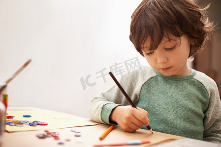 妈妈们不会喜欢这样的……一个可爱的小男孩在家里的桌子上画画。