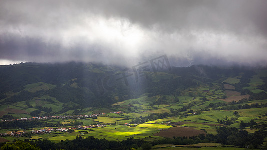明亮的阳光透过云洞照射到葡萄牙圣米格尔亚速尔群岛山脉的黑暗场景。
