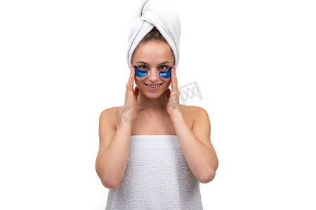 美丽的年轻女子在接受水疗护理后，头发上裹着毛巾，眼睛下面有蓝色的化妆品斑块