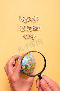 黄色背景上的木制字母的世界旅游日文字，手上拿着地球仪，还有放大镜