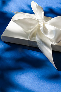 蓝色背景上带丝带和蝴蝶结的豪华假日白色礼盒、豪华婚礼或生日礼物