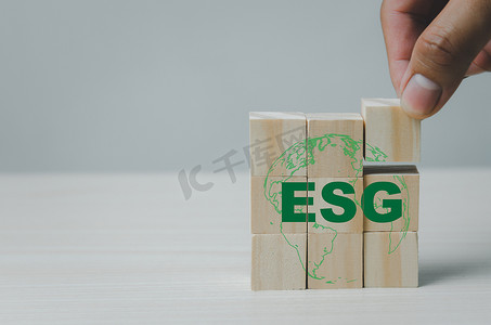 地球资源摄影照片_手工将带有 ESG 环境社会治理符号的木立方体放在桌子复制空间上。商业概念。