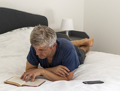 台灯看书摄影照片_照片中，一名中年男子躺在床上看书。