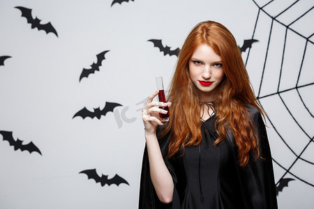 黑色蝙蝠摄影照片_万圣节女巫概念 — 快乐万圣节女巫在深灰色工作室背景下用蝙蝠和蜘蛛网喝血。
