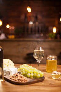 坚果拼盘摄影照片_老式酒吧的质朴木桌上摆着奶酪拼盘、新鲜葡萄和白葡萄酒。