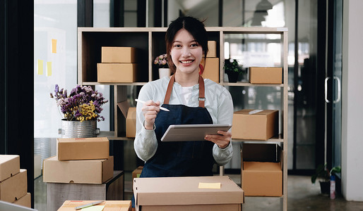 亚洲女性在包裹箱上写下客户的运输信息，她拥有一家网上商店，她通过一家私人快递公司将产品运送给客户。
