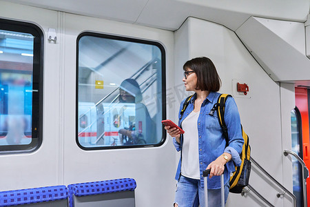 车内乘客摄影照片_带着手提箱背包的女乘客站在车内、通勤列车上