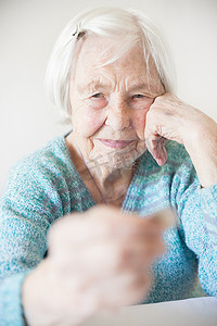 贫困老人摄影照片_悲伤的老妇人坐在家里的桌子旁，痛苦地看着手里只剩下养老金的硬币。