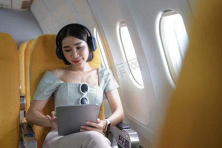 旅游与现代技术和航空概念，女性坐在飞机上与现代数字小工具和搜索最喜欢的音乐播放列表在应用程序中聆听