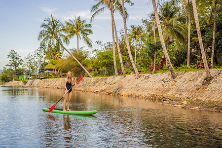 SUP 站起来桨板女人在湖上桨板快乐地站在蓝色水面上的桨板上。