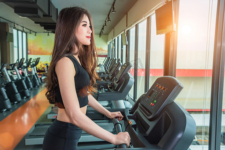 跑步女孩摄影照片_亚洲运动女性在健身健身房的跑步机设备上行走或跑步。