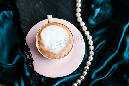 自助早餐摄影照片_一杯卡布奇诺早餐，配有缎子和珍珠珠宝背景，巴黎咖啡馆的有机咖啡和无乳糖牛奶，适合豪华复古度假品牌