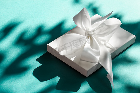 装饰礼物盒摄影照片_翠绿背景上带丝带和蝴蝶结的豪华假日白色礼盒、豪华婚礼或生日礼物