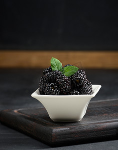 黑桌上的白色陶瓷盘里放着一堆成熟的黑莓
