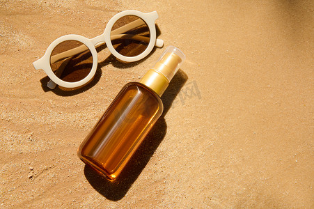 金色精华摄影照片_沙滩背景上装有 SPF 油或防晒润肤露和太阳镜的无品牌瓶子。
